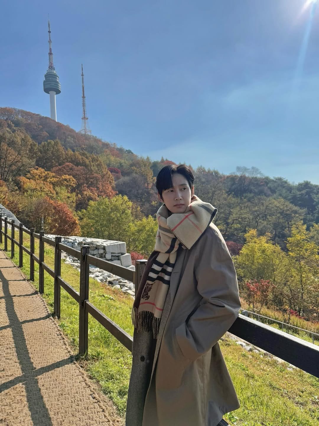 Photo shared by 박스아범 박성훈 on November 20, 2025 tagging @burberry. May be an image of duffle coat, overcoat, parka, outdoors, tower and text.