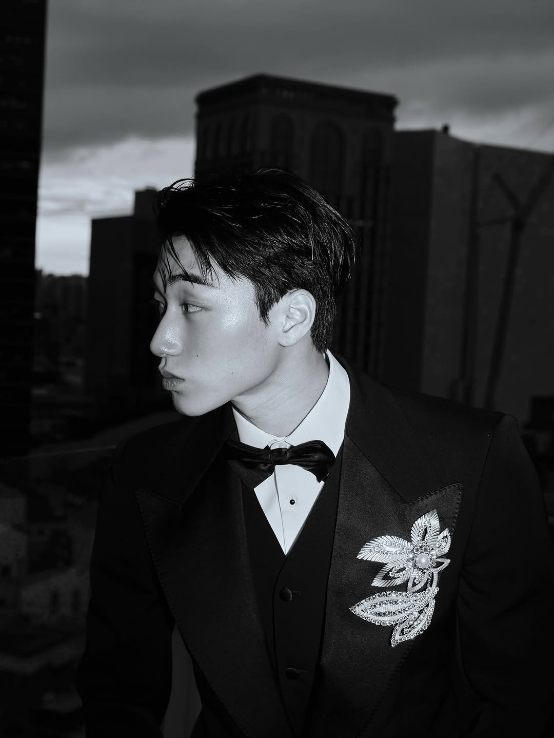 Photo shared by 산 (SAN) on October 15, 2025 tagging @dolcegabbana. May be a black-and-white image of suit, dinner jacket, blazer, bolo tie, bowtie and text.