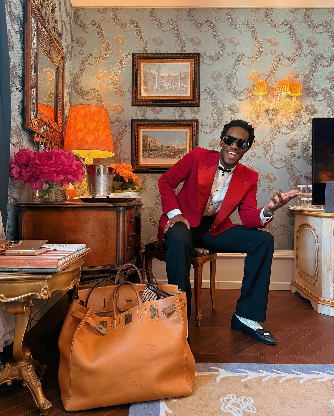 Photo shared by Wisdom Kaye on June 18, 2025 tagging @maisonvalentino. May be an image of 1 person, wingtip shoes, leather, eyewear, blazer, suit, briefcase and text.